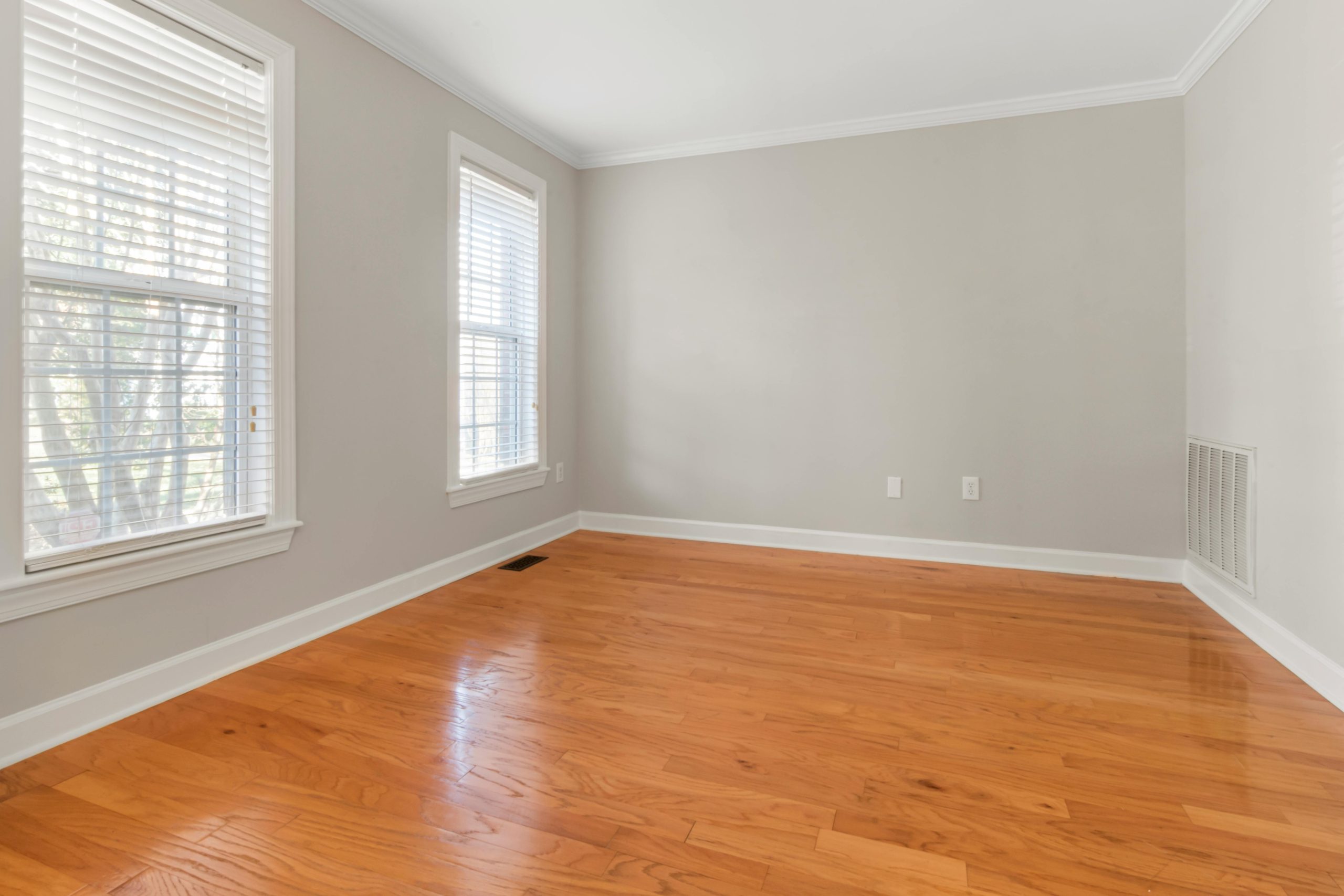 Spacious empty room with natural light, hardwood floors, and neutral walls.